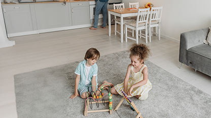 Ein Wohnzimmer voller Konsumgüter wie Spielzeug, Möbel und Küchenutensilien. Kinder spielen auf dem Teppich.